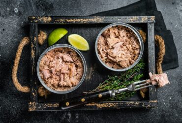 Open Can with Preserved tuna fillet meat. Black background. Top view